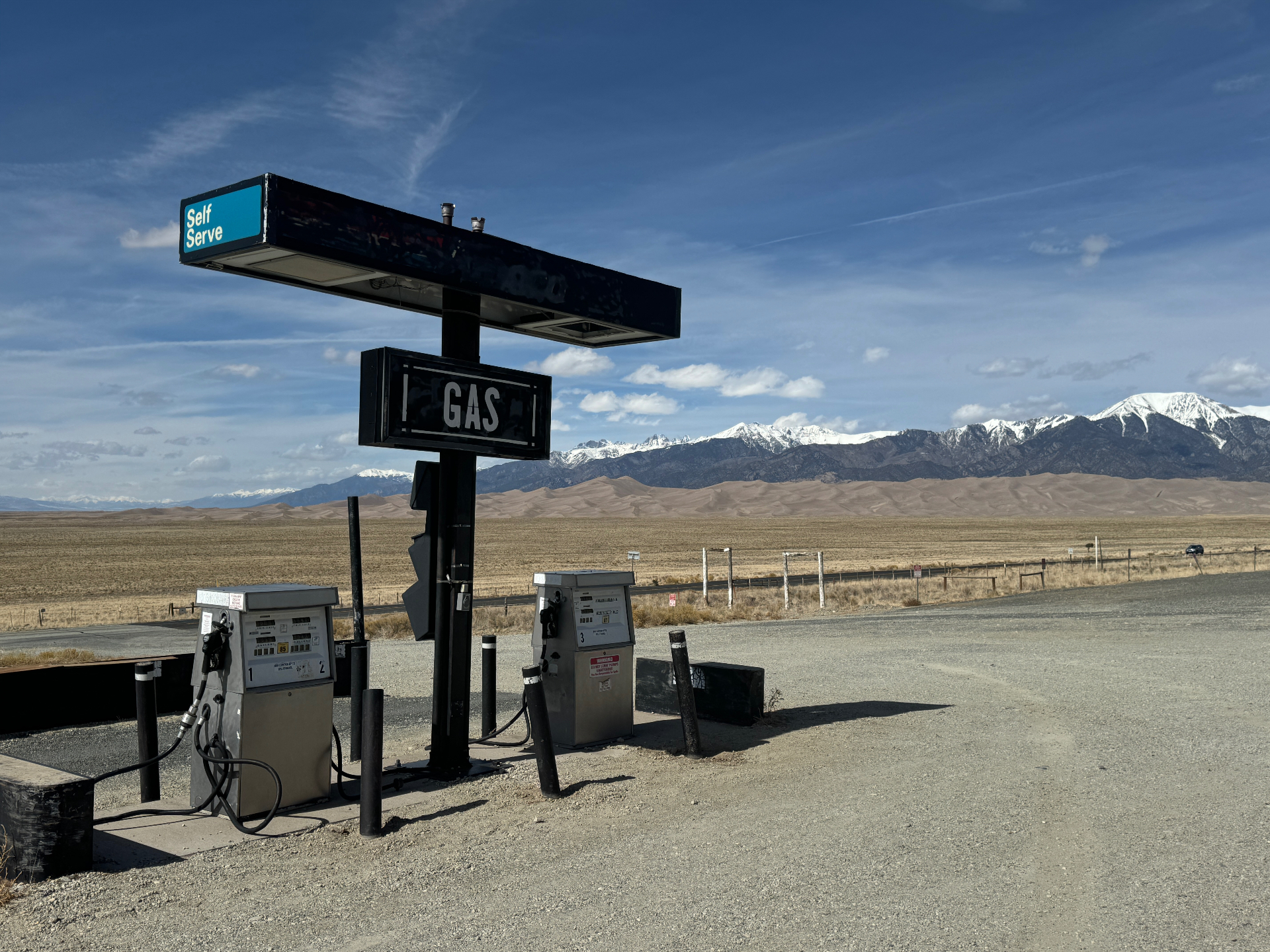 Historic self-serve gas station with dunes and snow-capped mountains in the distance