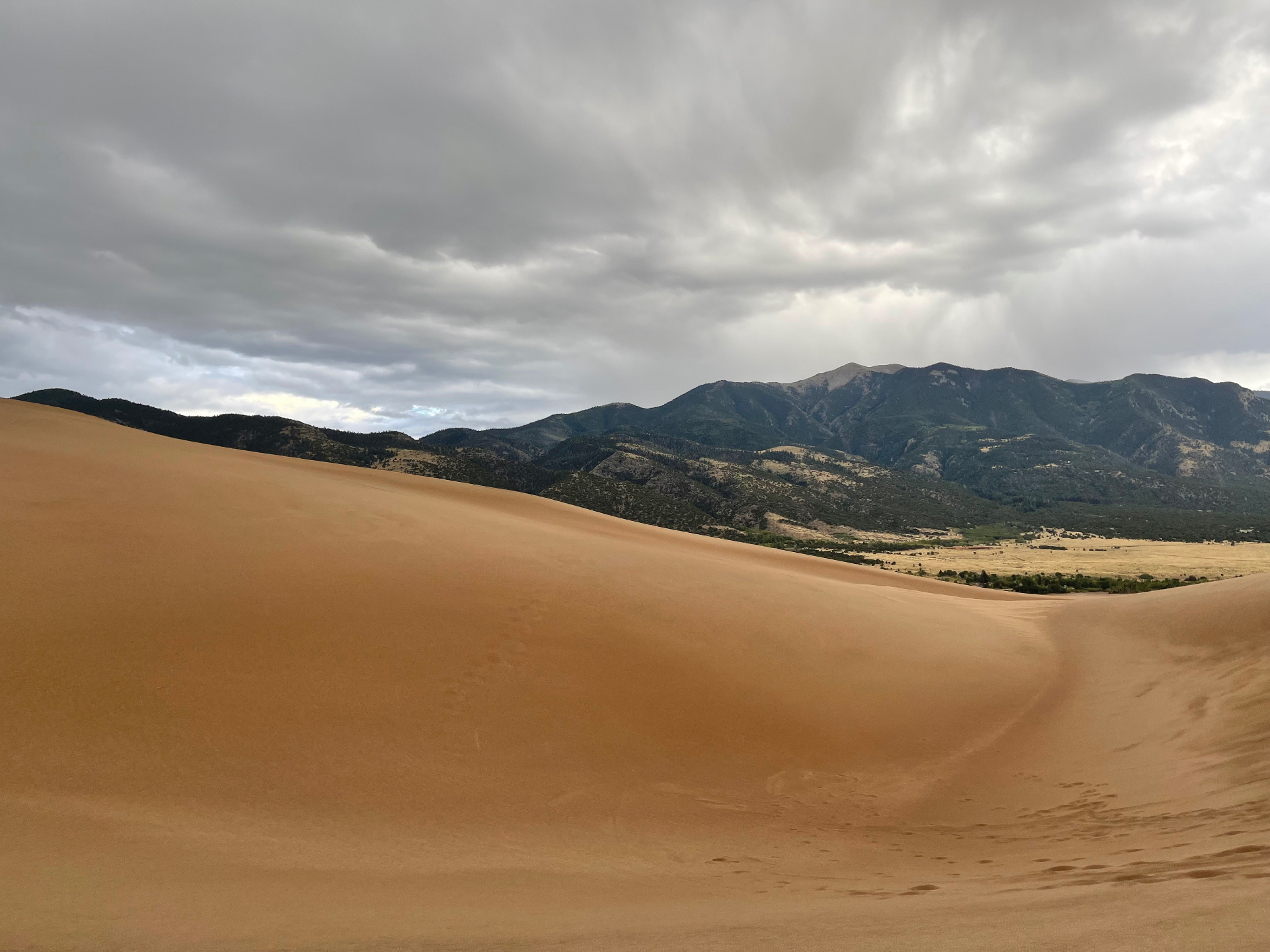 Great Sand Dunes under storm light with mountain backdrop